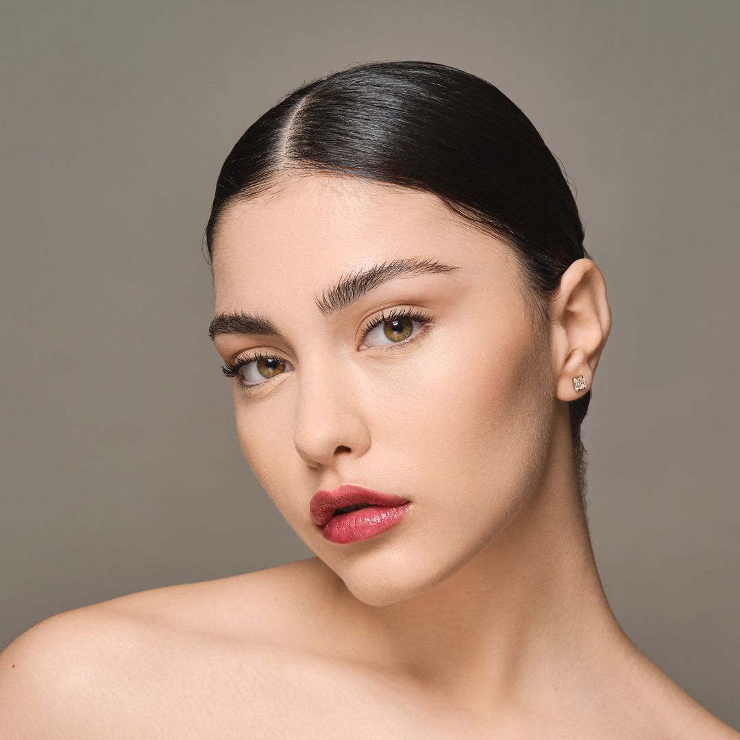 Baume lèvres Moniamori Supreme Lip Treatment Framboise posé sur un fond rosé élégant, révélant sa texture crémeuse et brillante.